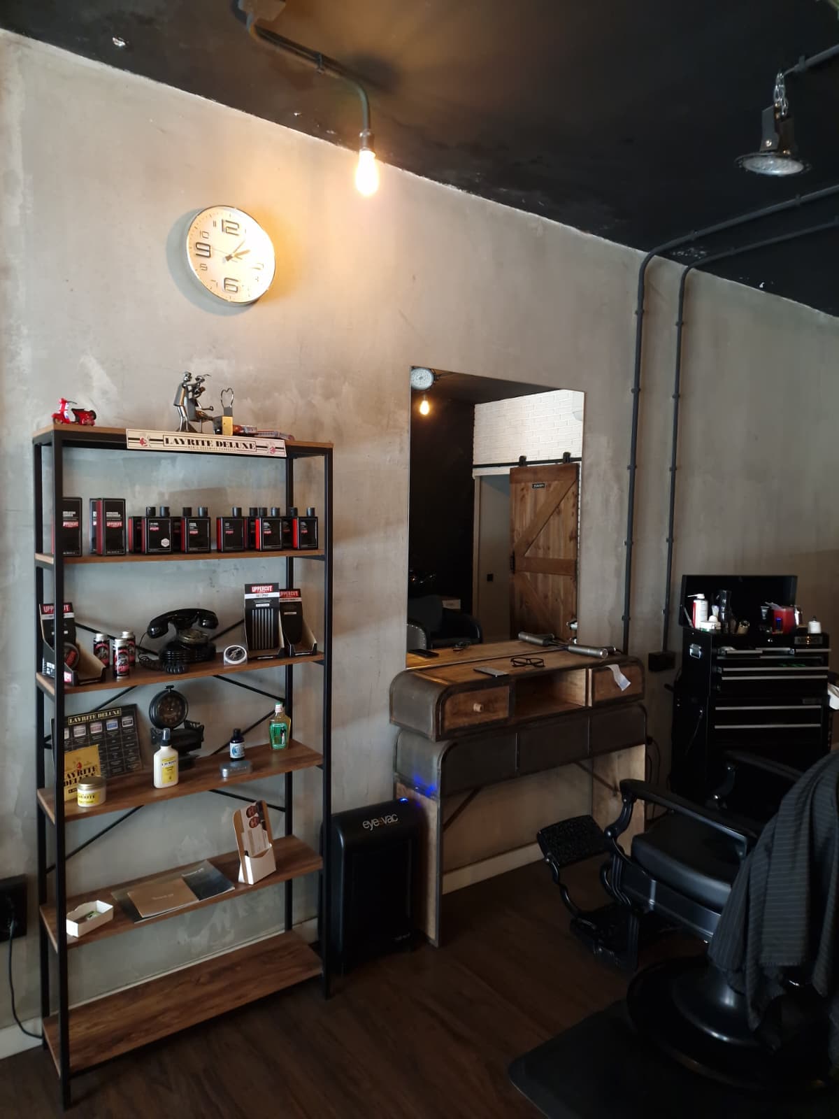 Estación de barbero de Sonrisa Canalla con espejo, mueble vintage y estantería con productos Layrite y Uppercut Deluxe